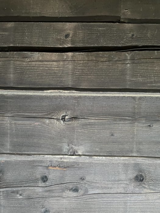 Svartmålad brädfasad med synliga sprickor och skarvar.