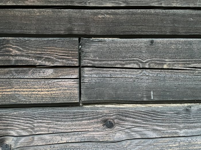 Närbild på en vägg med mörkbrun, horisontell brädfasad som visar åldrande och slitage.