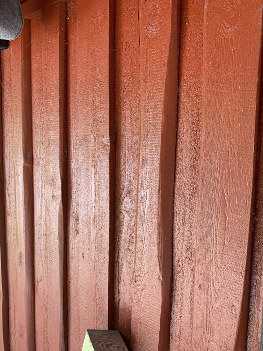 Stående träpanel med lockbräda och vankant målad i rött på ett hus.