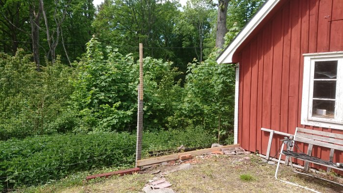 Ett pågående bygge av en enkel kattinhägnad med stolpar och nät vid ett rött hus med en ovanlig elinstallation synlig.