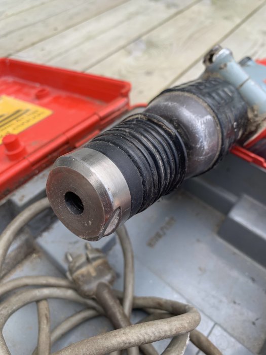 Närbild av en Hilti-borrmaskins fäste mot en suddig bakgrund av en röd verktygslåda och kablar.