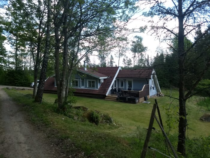 Ett enfamiljshus med ommålat träfasad och ny takbeläggning i en skogsglänta.