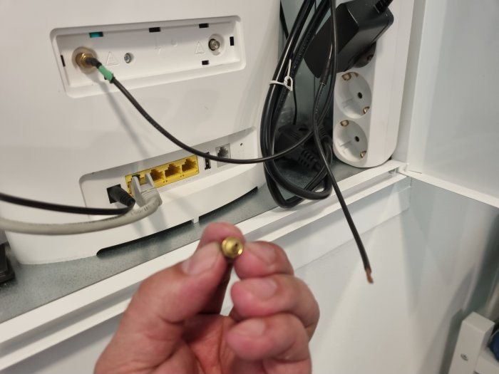 Hand håller en SMA-J-1.5 RF Coaxial Connector med avskalad kabel framför en gruppcentral.