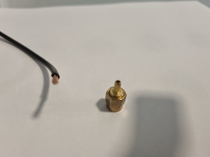 Kabel slut med kopparfiber bredvid en SMA-J-1.5 RF koaxialkontakt på vit bakgrund.