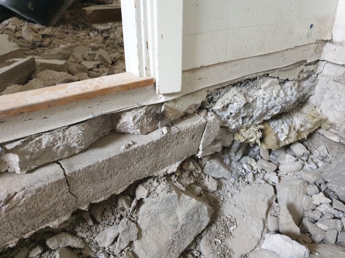 Mellanvägg av lättbetong synlig ovanför söndertagen betongplatta med grus och byggbråte.