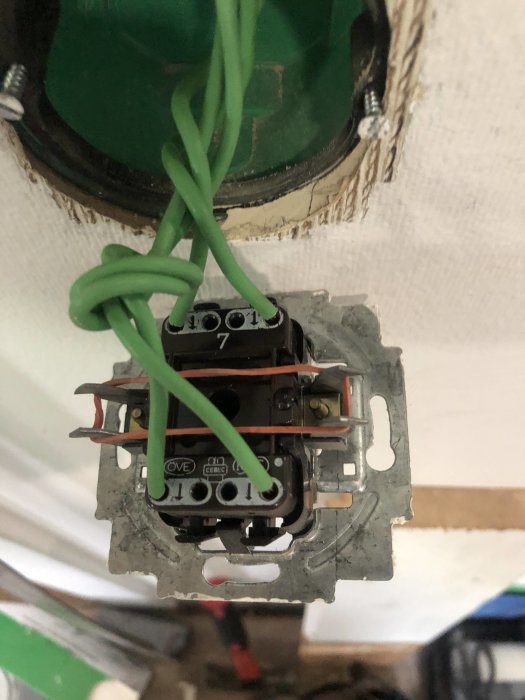 Elektrisk väggströmbrytare öppnad med synliga anslutningar och flera ihoptrasslade gröna kablar.