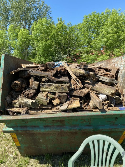 En fullastad container med gamla brädor och trädgårdsavfall på en solig dag.