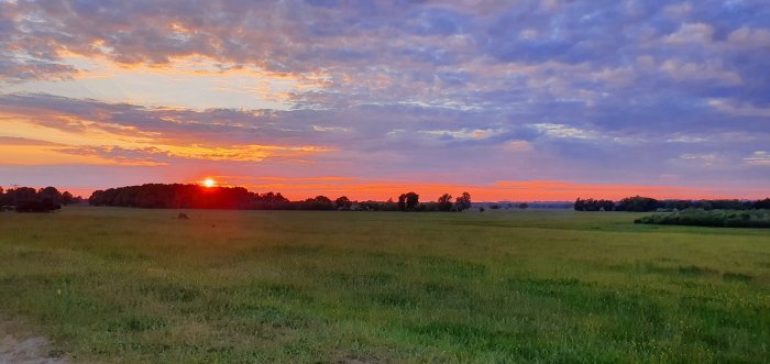 Solnedgång över ett öppet fält med dramatisk himmel i röda och blå toner.