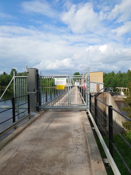 Slussport vid en vattenväg med stängt metallstaket och skylt med texten "Fortum Linghed Kraftstation".