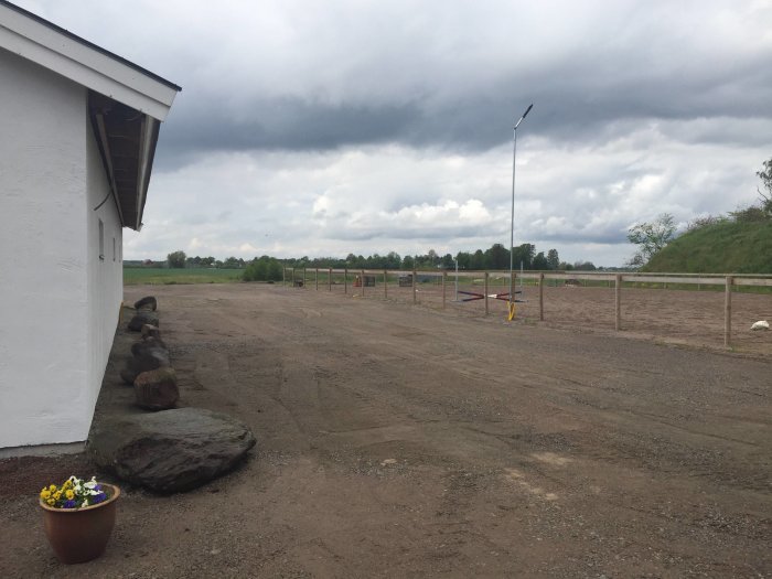 Verkstadens gavel med vitputsad vägg och lecablock, mot en bakgrund av mörka moln och landskap.