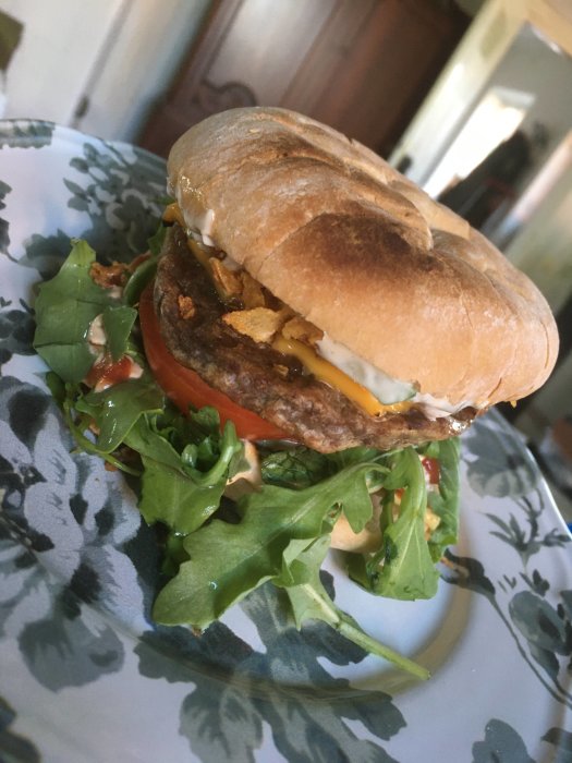 Grillad hamburgare med surdegsbröd, sallad, dressing och tomater på ett blommönstrat fat.