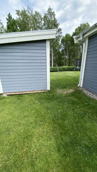 Gräsmatta mellan en huskropp och ett förråd som visar potentiell väg för en robotgräsklippares begränsningsslinga.