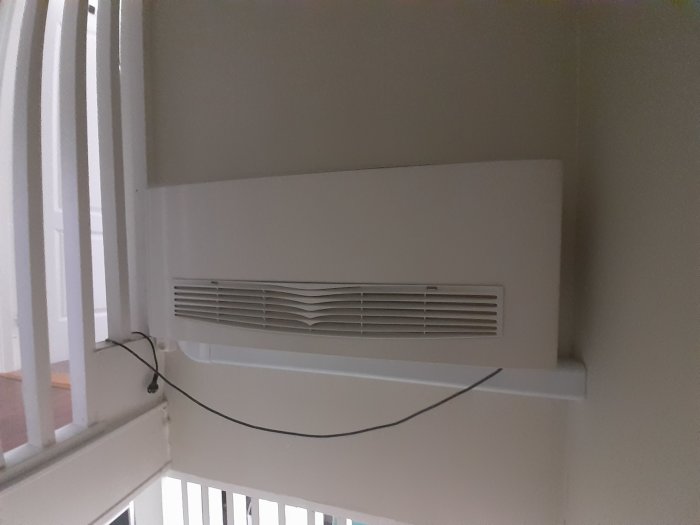 En airconditionenhet på väggen med elsladden hängande lös och kopplad till enheten.