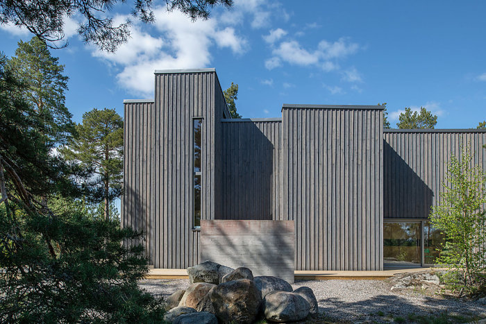 Moderna träbeklädda fasader på ett arkitektritat hus med stora fönster omgivet av träd och stenar.