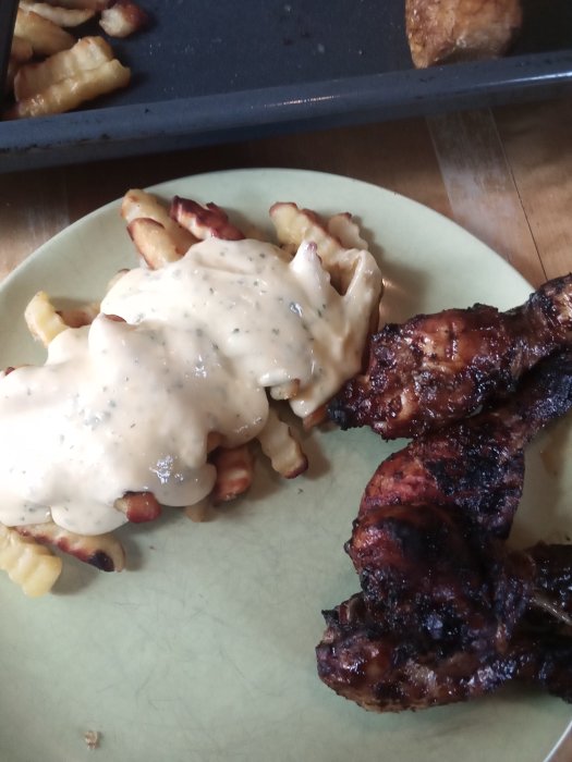 Pommes frites med bearnaisesås och grillade kycklingklubbor på en tallrik.