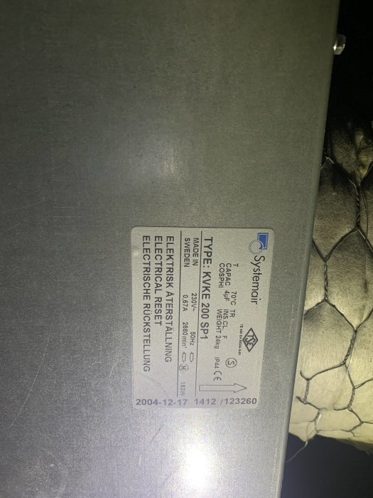 Bild på en etikett med teknisk specifikation på en elektrisk enhet, tagen i svagt ljus.