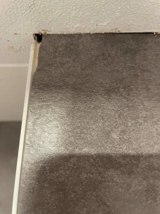 Avskalad kant av våtrumsmatta i hörnet från golv till tak som visar en glipa.