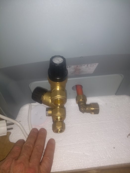VVS-installation med termostatventil på vit bakgrund, med hand för storleksjämförelse.