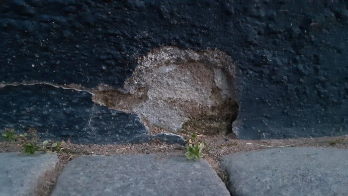 Skada på en målad sockel med ett hål och sprickor bredvid en trottoarkant.