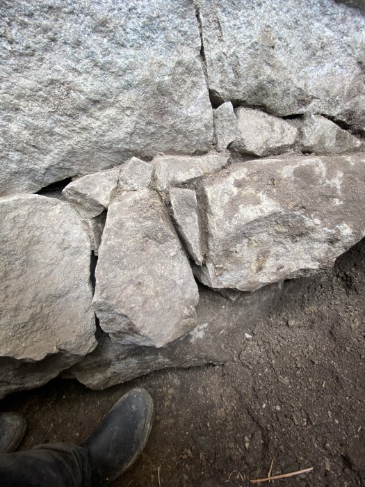 Kallmurad stengrund med synliga fogar och jord, en person i svarta skor syns delvis.