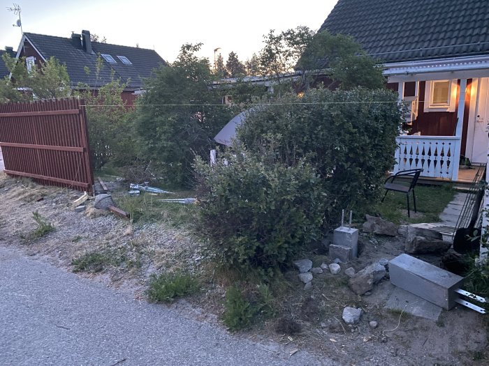 Trädgård med brutet staket och cementklump vid ruttnad stolpe, stenar på marken.