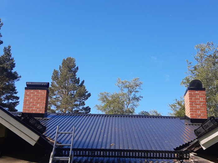 Två nyligen omurnade skorstenar på ett hus med blått plåttak mot en klarblå himmel.