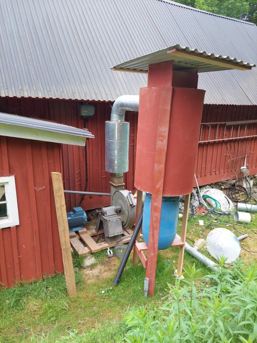 Cyklonseparator för spånhantering monterad utomhus vid röd byggnad med rörmotor och blå behållare.