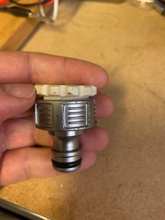 Hand håller en vit adapter monterad på en metallisk krankoppling mot ett bord.