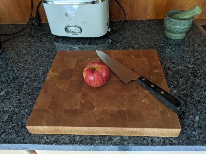 Ändträskärbräda av spillbitar på köksbänk med äpple och kniv.