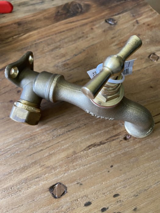 Mässingsvattenutkastare med väggfäste och kran ej korrekt monterad på ett träbord.