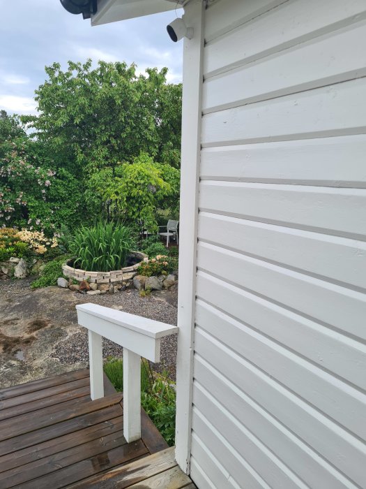 Hörnet av ett vitt trähus med en trätrall och knutbrädor som möts, med synliga tecken på slitage vid nedre kanten.