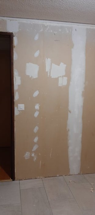 Vägg i källarrum med borttagen tapet och ojämnheter, delvis spacklade inför renovering.
