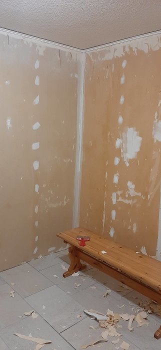 Renoverat rum med blottade gipsskivor på väggarna och avskalad tapet på golvet.