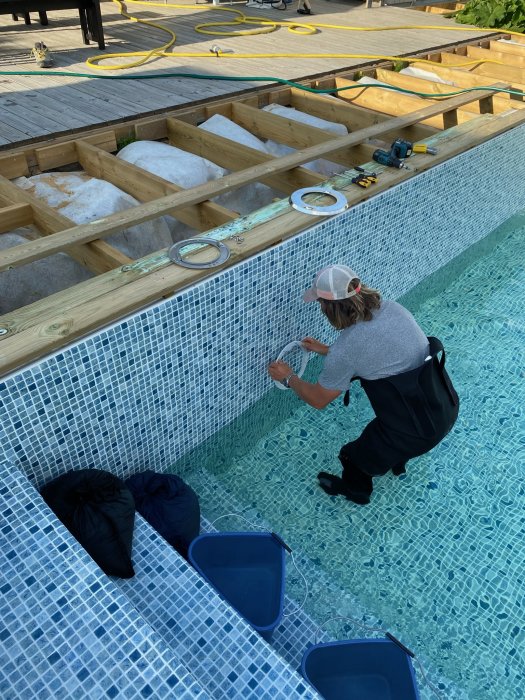 Poolbyggare arbetar med installation i en halvfylld pool med kaklade väggar och genomskinligt vatten.