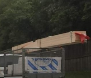 Trave av brädor säkrad med ett band på ett släpvagnsgaller med röd varningsflagga.