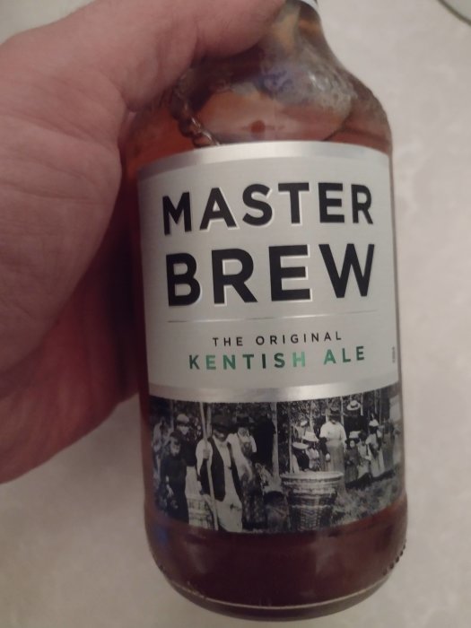 Hand håller en flaska Master Brew Kentish Ale med etikett som visar historisk bild.