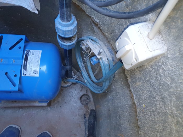 Vattenpump och hydropress i brunn med anslutna rör och kablar synliga.