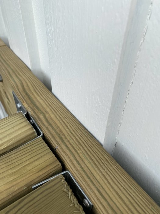 Detaljbild av trallplåt mot vit fasad, balkongram och reglar synliga med glipa intill fasaden.