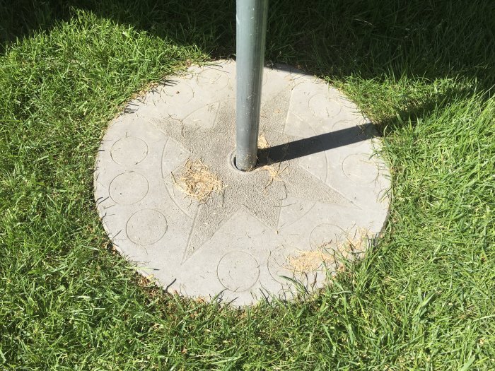 Egengjuten cirkulär betongplatta med hål för stolpfäste på gräsmatta.
