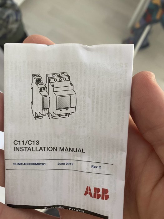 Hand håller en installationsmanual för elmätare från ABB, med en teknisk ritning på omslaget.