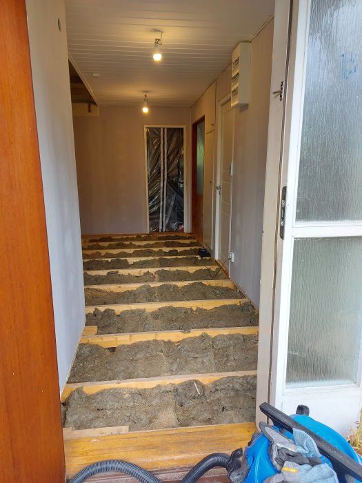 Renoveringsprojekt med upptaget golv och synliga golvbjälkar i en korridor.