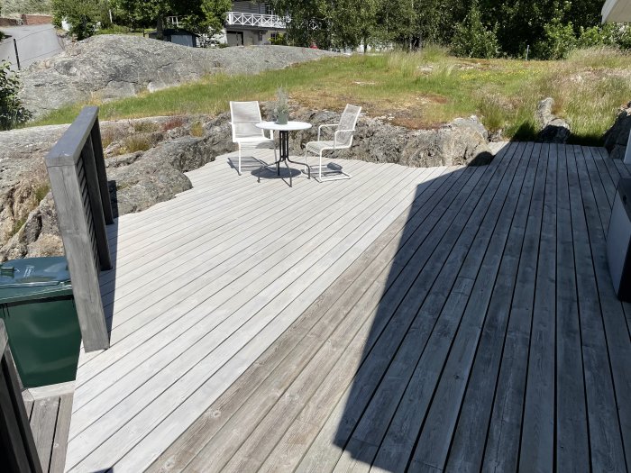 Nybehandlad trall på altan bredvid obehandlad del, med trädgårdsmöbler och berg i bakgrunden.