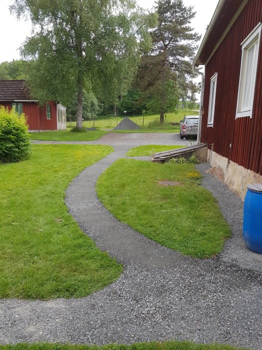 Grusgång som slingrar sig från en röd trähus entré upp till en parkeringsplats med grönområden runtomkring.