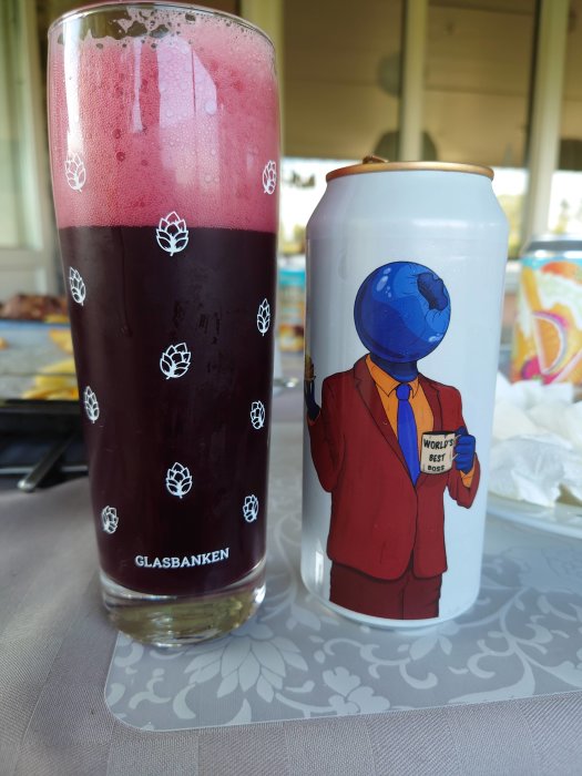 Ett glas med mörk dryck och rosa skum bredvid en burk med illustration av karaktär som håller i en mugg.