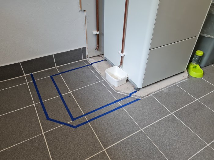 Golv med markerad yta för ny klack intill befintlig värmepump för varmvattenberedare.