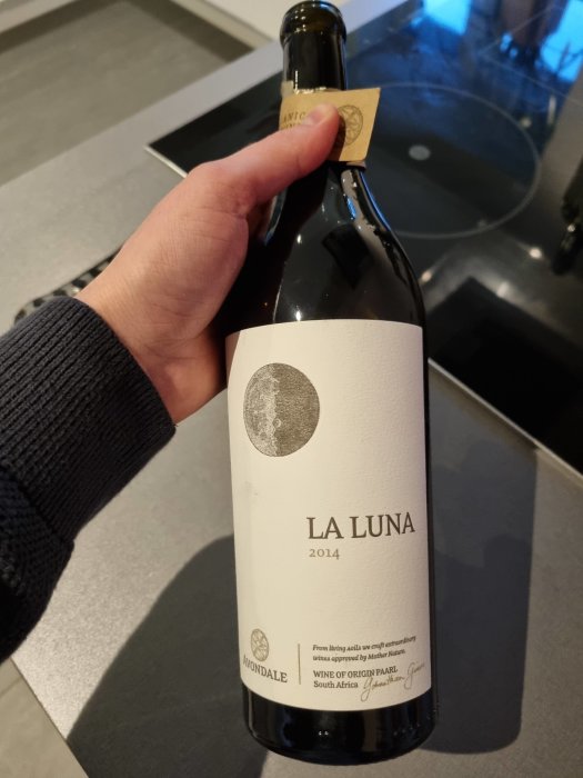 En hand håller en flaska vitt vin, La Luna 2014 från Avondale, Sydafrika.