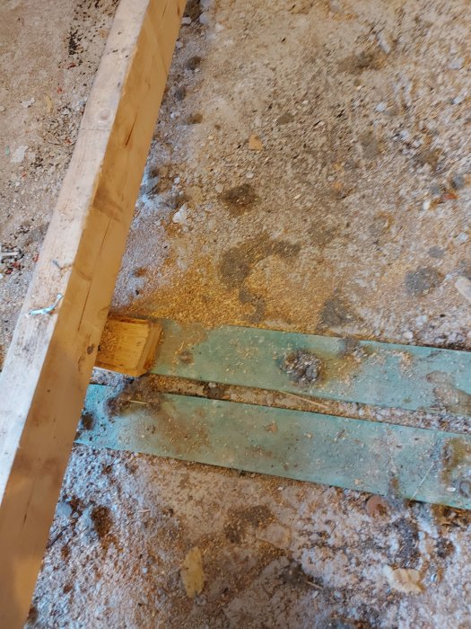Renoveringsarbete med en synlig regel, sågspån och gamla spikreglar på ett betonggolv.