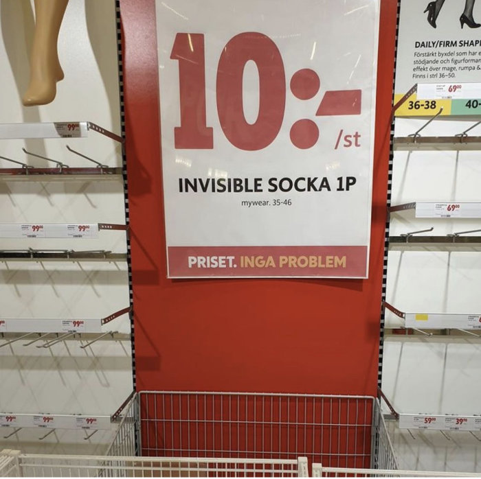 Tomma hyllor med skylt för "invisible socka 1p" och priset 10 kronor, i en butik.