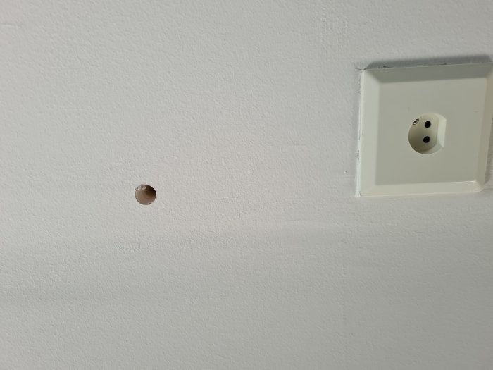Vitt tak med ett större hål och eluttag, behov av reparation och spackling beskrivs.