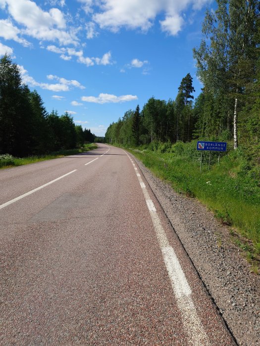 Asfalterad landsväg med skylt som anger infart till Borlänge kommun, omgivet av grönska under blå himmel.